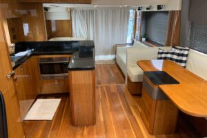 2016 Sunseeker Manhattan 65 salon with cream upholstery, teak accents, and panoramic windows overlooking the water.