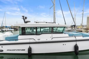 2023 Axopar 37 XC Cross Cabin bow seating area with forward-facing helm station and windscreen viewed from starboard side.